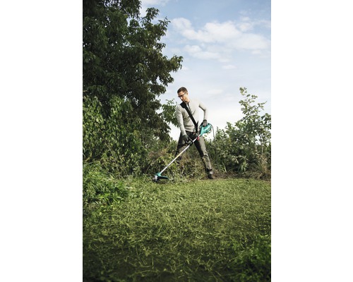 En man använder en grästrimmer i en trädgård för att klippa gräsmattan.