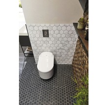 Modernt badrum med en vit toalett, hexagonala plattor på vägg och golv samt ett väggelement i trä.