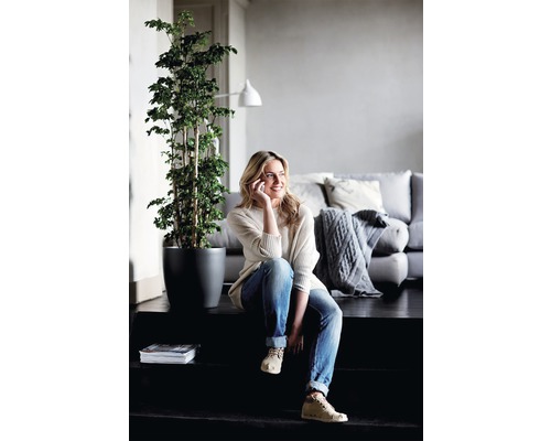 Kvinna sitter på trappan med krukväxt, telefon, tidning och soffa i bakgrunden