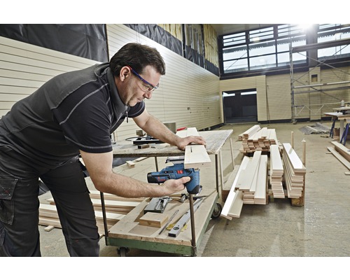 En man använder en sticksåg för att såga en träplanka.