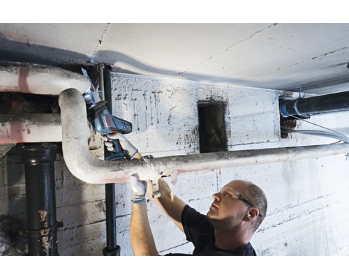 En man sågar ett rör i en källare med en sladdlös tigersåg.