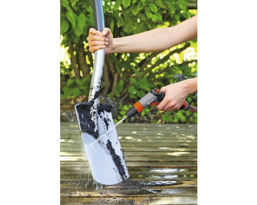 En person rengör en spade med en vattenstråle på en träyta.
