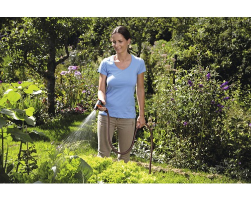 Kvinna vattnar trädgård med trädgårdsslang och sprutpistol