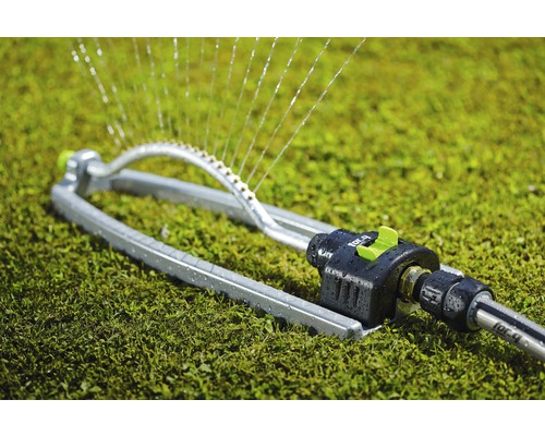 Oscillerande trädgårdsspridare i metall på gräsmatta med vattenspraystrålar