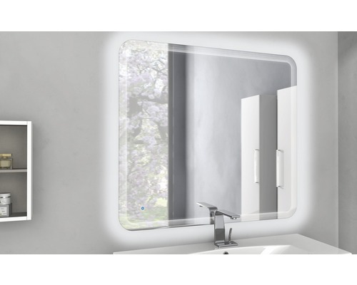 Belyst badrumsspegel ovanför ett handfat med kran i ett badrum.