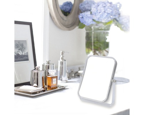 Badrumsscen med sminkspegel, tvålpump och dekorativa föremål på en vit yta