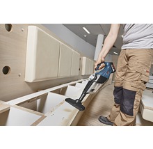 En person använder en sladdlös dammsugare för att rengöra en trädhylla.