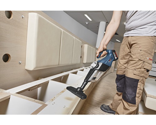 En person använder en sladdlös dammsugare för att rengöra en trädhylla.