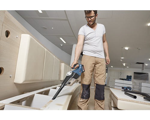 Man suger spån från en möbel med en batteridriven dammsugare.