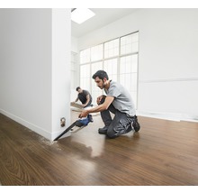 Två hantverkare lägger laminatgolv med en sänksåg i ett ljust rum.