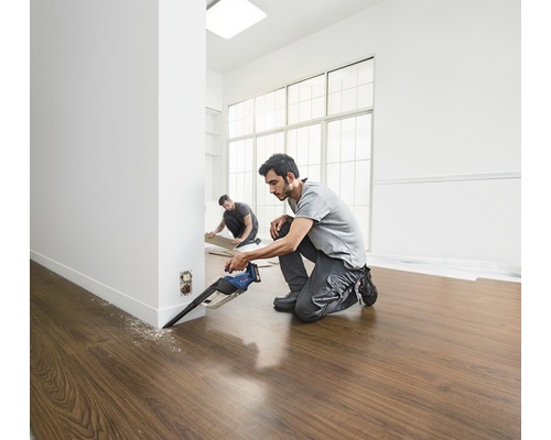 Två hantverkare lägger laminatgolv med en sänksåg i ett ljust rum.