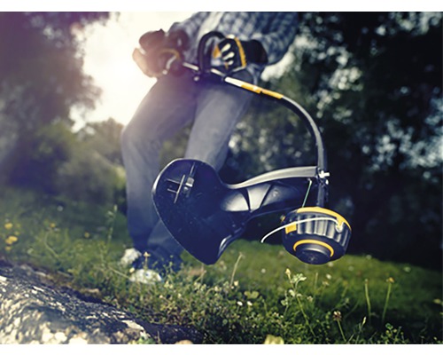 Person använder en grästrimmer i trädgården.