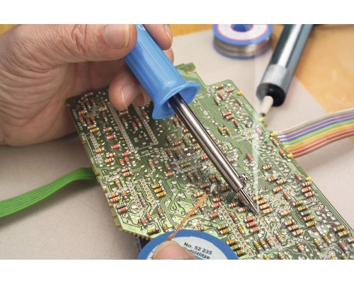 En person löder ett kretskort med en lödkolv. Lödtenn finns också.