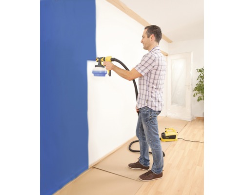 En man använder en färgspruta för att måla en vägg i ett rum.