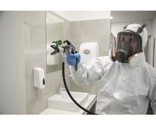 En person i skyddskläder använder en färgspruta i ett badrum.