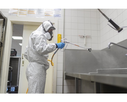 En person i skyddskläder sprutar en yta med en spruta