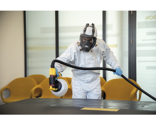 En person i skyddskläder desinficerar ett rum med en spruta.
