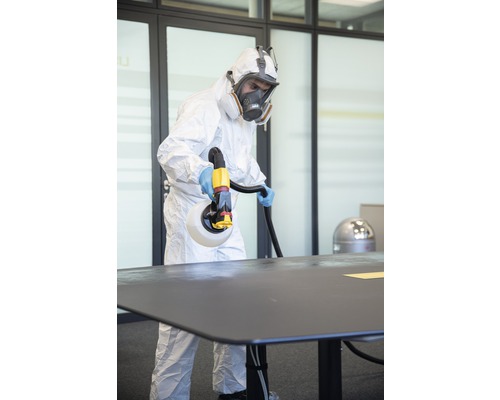 En person i skyddskläder desinficerar ett bord med en desinfektionsspruta.