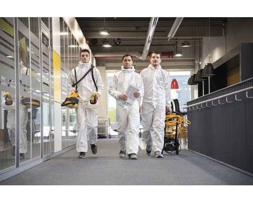 Tre personer i skyddsdräkter går på ett kontor.