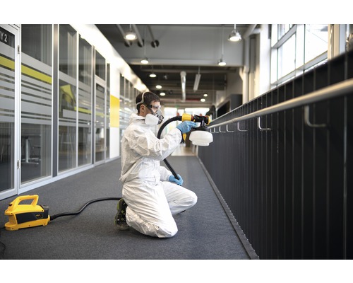 Man i skyddsdräkt desinficerar ett räcke inomhus med en spruta.