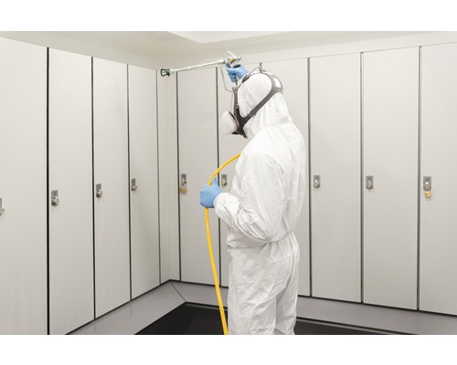 Man i skyddskläder desinficerar skåp med spruta