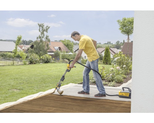 En man behandlar en träterrass med ett Wagner färgspraysystem i trädgården.