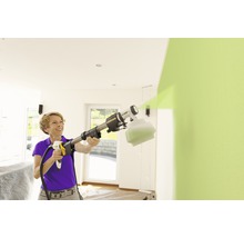 Kvinna använder färgspraysystem för att måla en vägg inomhus.