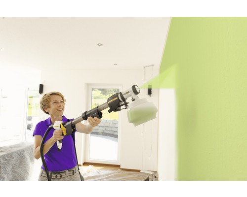 Kvinna använder färgspraysystem för att måla en vägg inomhus.