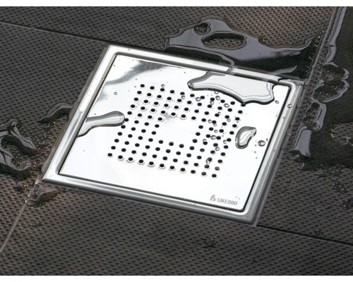 Fyrkantigt Smedbo golvbrunn av metall på mörk bakgrund med vattendroppar