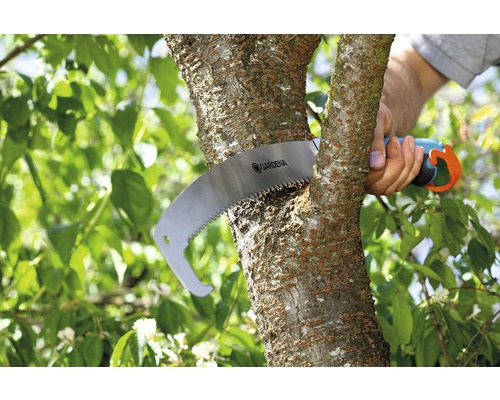 En person sågar av en gren med en handsåg av märket Gardena.