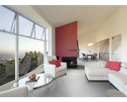 Vardagsrum med stort fönster, fåtölj, soffa, matta och öppen spis.