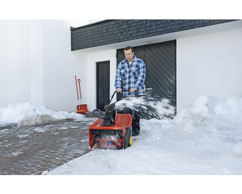 Man röjer snö med en snöslunga framför en byggnad.