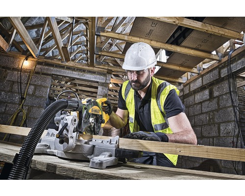 En man med skyddshjälm och varselväst använder en DeWalt kap- och geringssåg för att såga trä