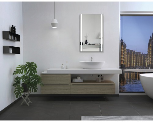 Modernt badrum med handfat, belyst spegel och badkar framför ett fönster