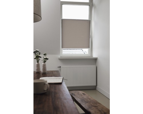 Miljöbild med plisségardin vid fönstret, bord, sittbänk och element