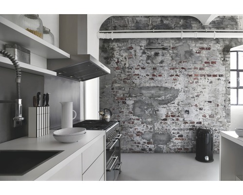 Ljust kök med pentry, fläkt, spis, köksredskap och papperskorg framför en tegelvägg.