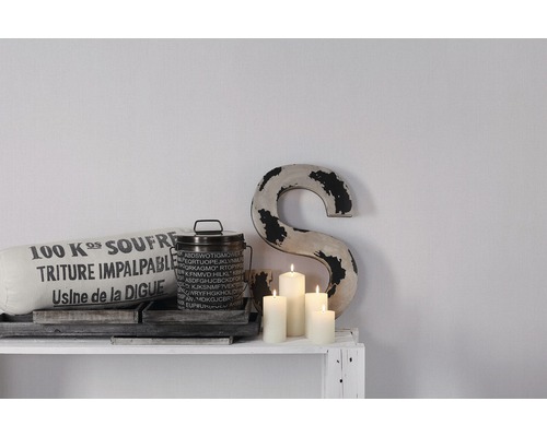 Dekorativ scen med kudde, burk, ljus och en bokstav på en hylla