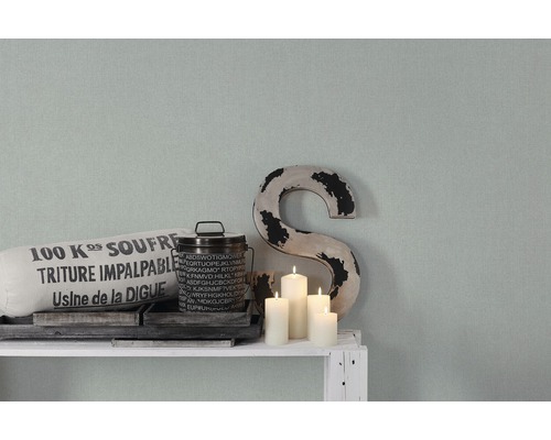 Dekorativ scen med kudde, burk, ljus och ett ''S'' på en hylla