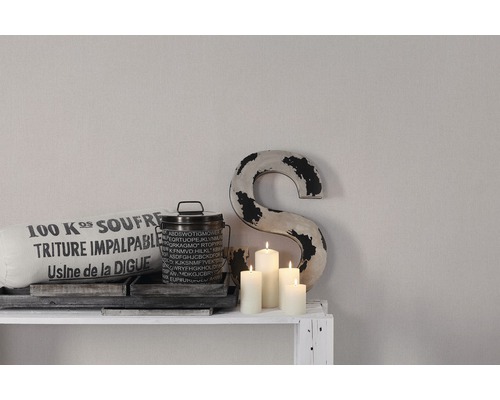 Dekorativ scen med kudde, burk, ljus och dekorativ bokstav på en hylla