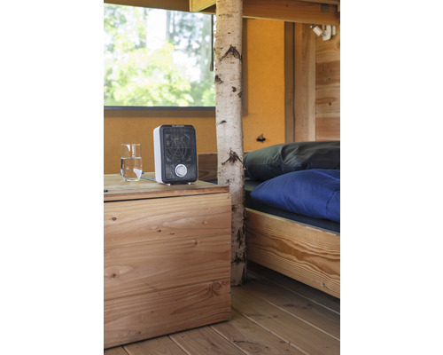 Interiör med säng, trägolv, nattduksbord, vattenglas och värmefläkt