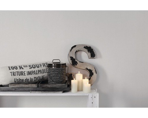 Dekorativ scen med kudde, burk, ljus och bokstavsdekoration på en vit hylla.