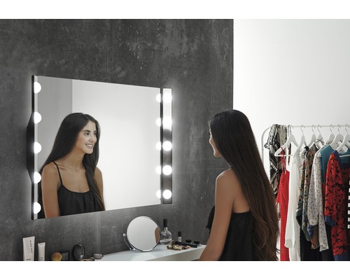 Kvinna framför en upplyst sminkspegel i badrummet.