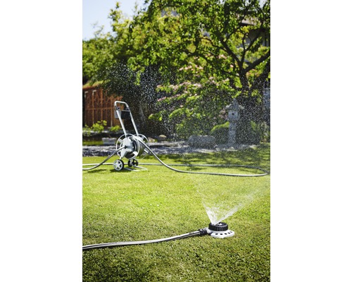 Trädgårdsscen med grässpridare och slangvagn för bevattning