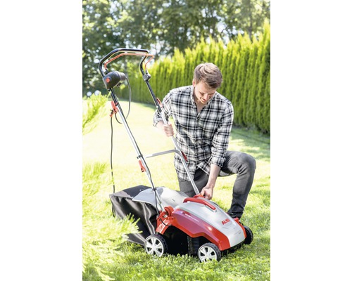 Man använder en gräsmattluftare i trädgården. Enheten har en uppsamlingskorg.