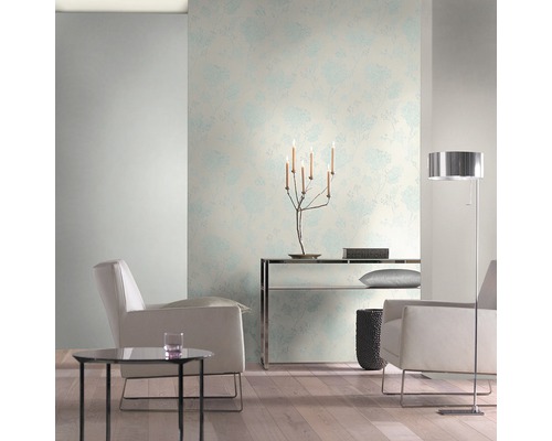 Ljust vardagsrum med blommönstrad tapet, fåtöljer och golvlampa.