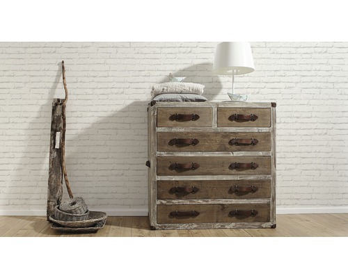 Träbyrå med sex lådor, dekoration och lampa framför en tegelvägg