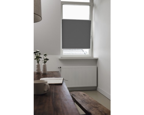 Vy över ett rum med ett fönster försett med en grå plisségardin, tillsammans med ett träbord och en bänk