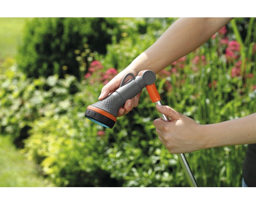 Trädgårdsslang med spruthuvud i handen framför gröna växter