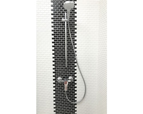 Duscharmatur med handdusch framför vägg med svarta och vita plattor