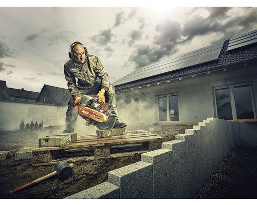 En man med hörselskydd och skyddsglasögon skär en sten med en stensåg på en byggarbetsplats.